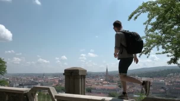 Чоловік, який подорожує з рюкзаком, досліджує місто, дивлячись на панорамний вид на місто та узбережжя. Концепція подорожей відкриває нові місця . — стокове відео