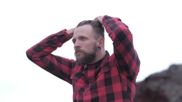 Красивый бородатый хипстер со стильной стрижкой и бородой с ножницами в красной клетчатой рубашке — стоковое видео