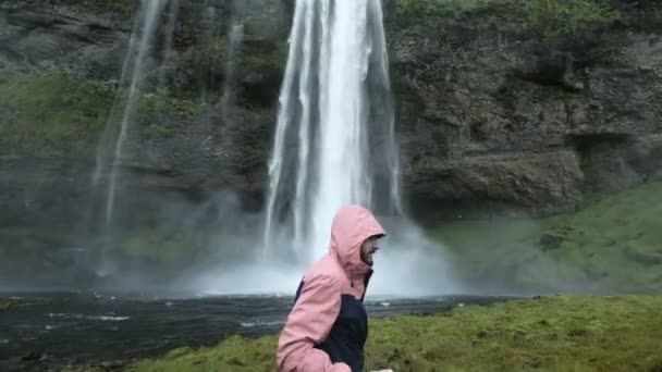 Kırmızı ceketli turist adamı anlamına gelir ve düşen su akışı görünüyor. Doğada Güzellik — Stok video