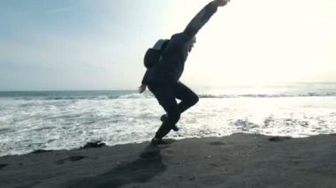 Siyah kumlu bir plaj üzerinde bir dağ üzerinde yürüyen genç adam. Tatil sırasında sıcak giysiler adamdır. Bir yürüyüş kıyıda bir kişidir