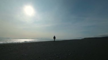 Siyah kumlu bir plaj üzerinde bir dağ üzerinde yürüyen genç adam. Tatil sırasında sıcak giysiler adamdır. Bir yürüyüş kıyıda bir kişidir