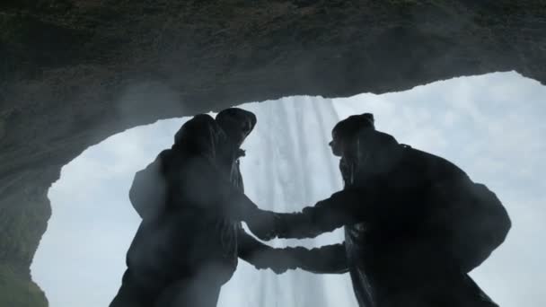 Ζευγάρι στέκεται πάνω σε λόφο στο καταρράκτη. Σιλουέτα ενός ζευγαριού κρατά τα χέρια — Αρχείο Βίντεο