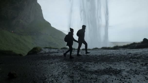 Para stoi na wzgórzu przy wodospadzie. Sylwetka para trzyma ręce — Wideo stockowe