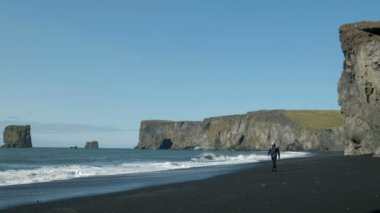 İzlanda'daki kıyı siyah kum plaj boyunca yürüyen adam bir sırt çantası ile