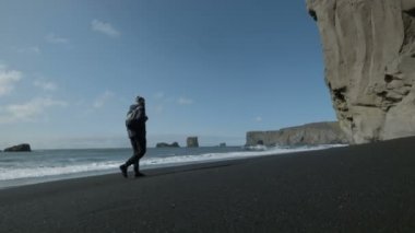 İzlanda'daki kıyı siyah kum plaj boyunca yürüyen adam bir sırt çantası ile