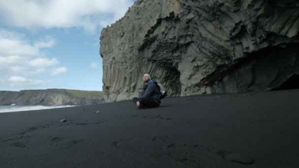 Человек сидит у темного моря - зимние пейзажи из Исландии — стоковое видео