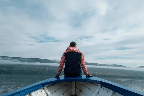 Nuori mies istuu veneessä vuoristojärven pohjalla. . — kuvapankkivalokuva