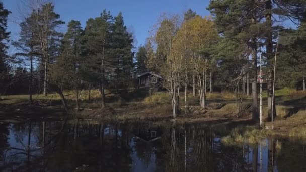 Pequeña casa de madera cerca del borde de un pequeño río o estanque en medio de un frondoso follaje, acercándose a la puesta de sol . — Vídeos de Stock