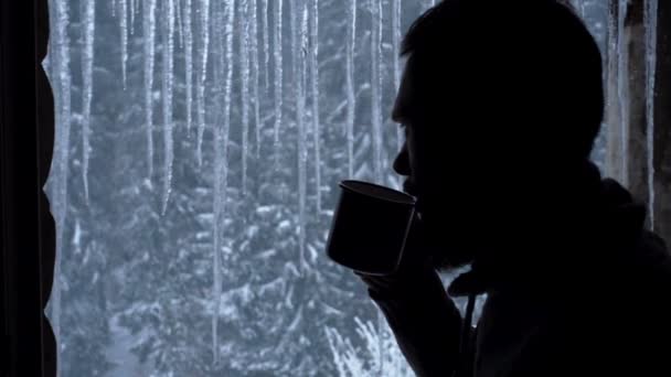 Красивий чоловік п'є з чашки, дивлячись з вікна зсередини будинку, в чорній сорочці . — стокове відео
