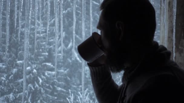 Un bel homme buvant dans une tasse regardant par la fenêtre de l'intérieur de la maison, portant une chemise noire . — Video