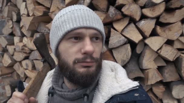 Человек дровосек с топором на фоне кучи дров — стоковое видео
