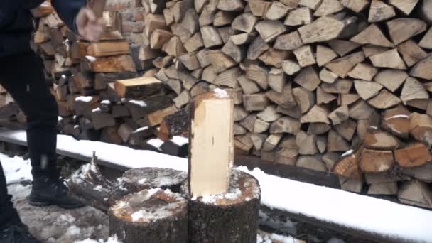 Повільний рух красивий молодий чоловік обробні лісу з сокирою біля будинку взимку — стокове відео