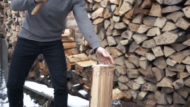 Mouvement lent d'un beau jeune homme coupant du bois avec hache près de la maison en hiver — Video