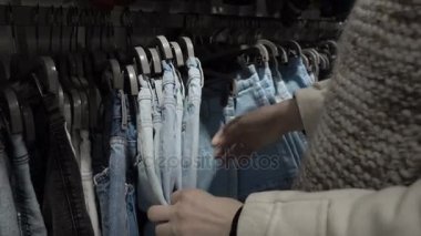 Elinde yeni giysiler, askı askı üzerinde farklı rahat renkli giysiler ile bakarak seçmek genç güzel kadın moda alışveriş merkezinde alışveriş yakın çekim