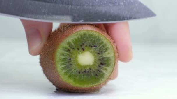 Kiwi siendo cortado en rodajas por la mitad sobre fondo blanco húmedo. de cerca — Vídeos de Stock