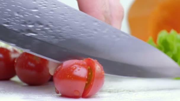 Cutting red cherry tomatoes with kitchen knife on white board, white background, close up footage 4K — Stock Video