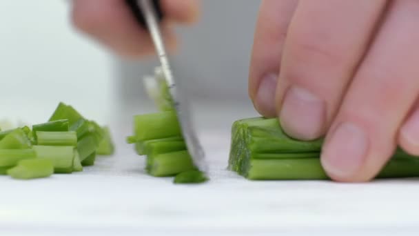 Cortar las cebollas verdes con un cuchillo en el tablero. Corte verde sin manos en el marco. El chef corta los ingredientes para la sopa. De cerca. — Vídeo de stock