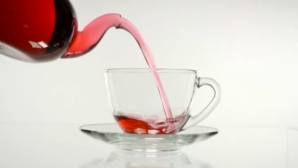 thé rose rouge dans une théière en verre et une tasse sur un fond blanc .