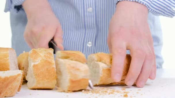 Manos de mujer cortando pan en la cocina. Primer plano de las manos femeninas sosteniendo el cuchillo, rebanando baguette blanca en la tabla de cortar. Cocinar en casa — Vídeo de stock