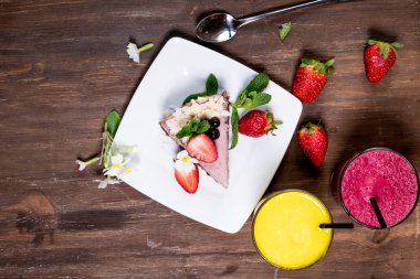 Eski ahşap masaya içki içtiğim için elini tutan bir bardak portakal ve Frenk üzümü suyu sabah üstten görünüm günlük taze kahvaltı. çilekli turta bir plaka üzerinde