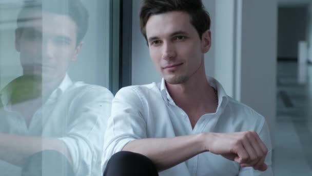 Porträtt av en stilig man i en vit skjorta som tittar ut genom fönstret. — Stockvideo