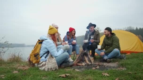 Grupo de amigos sorridentes sentados em torno da fogueira no acampamento — Vídeo de Stock