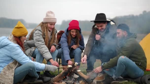 배고픈 여행자들은 마시멜로를 불로 요리하고 모닥불 주위에서 대화하는 동안 막대기로 먹는다, — 비디오