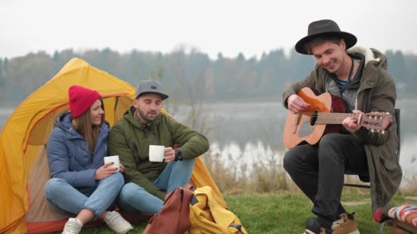 Grupo de amigos acampar. Eles estão sentados em torno de fogo acampamento, tocando guitarra — Vídeo de Stock