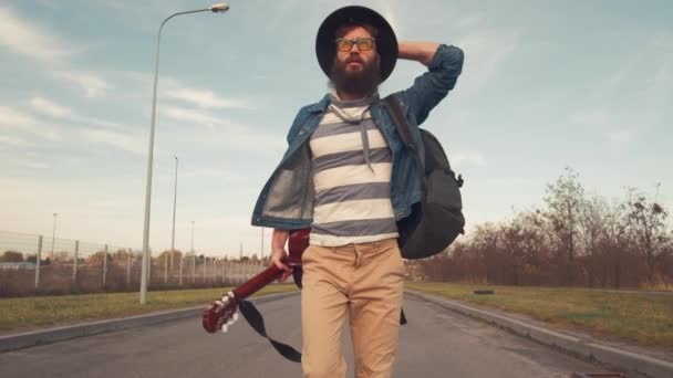 Портрет бородатого музыканта с тёплыми тёплыми глазами, гуляющего по парку в солнечный день с гитарой — стоковое видео