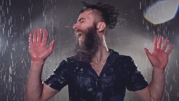 Attraente giovane uomo in vestiti neri bagnati sotto la pioggia e spruzzi d'acqua — Video Stock