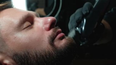 Berber müşterilerin sakallarını sandalyede tıraş eder. Sakal tıraşı. Elektrikli jiletle sakal tıraşı olan bir berber. Gerçek bir erkeğin tımarı
