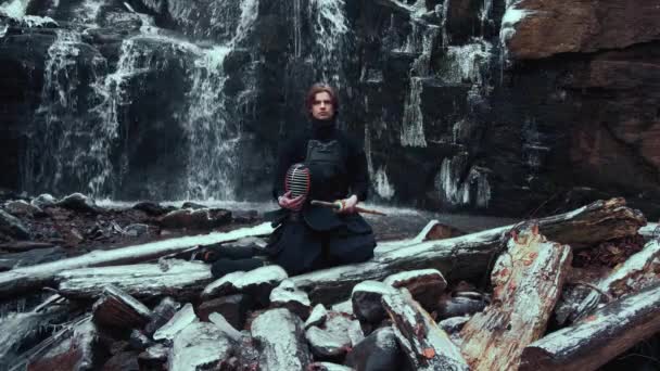 Mann übt Meditation mit Bambusschwert auf winterlichem Wasserfall-Hintergrund. — Stockvideo