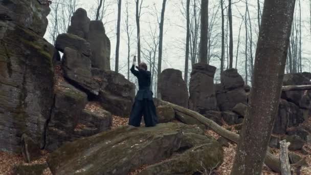 Uomo in abiti tradizionali giapponesi, con una spada, una katana, allena arti marziali sullo sfondo della foresta — Video Stock