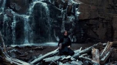 Şelale arka planında bambu kılıcıyla kendo çalışan bir adam.