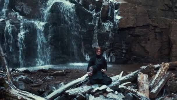 Чоловік практикує кендо з бамбуковим мечем на фоні водоспаду — стокове відео