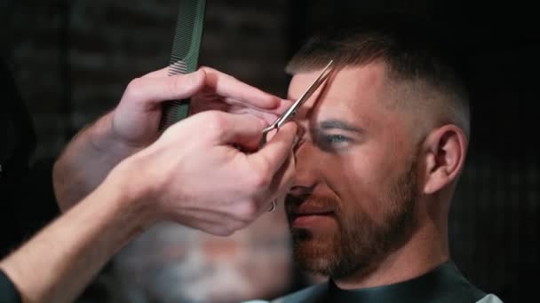 Corte de cabelo Mans por barbeiros tesoura e pente com logotipo da barbearia atrás em câmera lenta. Mans mãos fazendo corte de cabelo masculino no salão — Vídeo de Stock