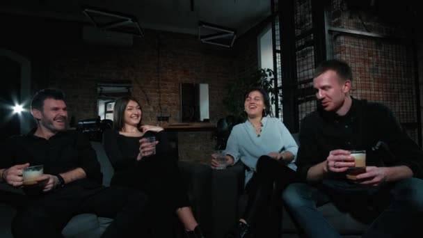 Un grupo de hipsters de cuatro amigos están sentados en un sofá. Beber bebidas — Vídeo de stock