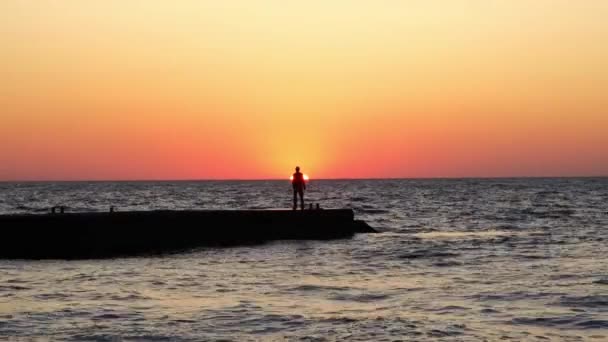 Een eenzame man bij zonsopkomst. Een man op het strand ontmoet de dageraad. zeegolf — Stockvideo