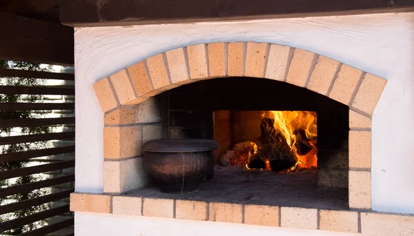 Una olla de sopa cerca de la leña. El fuego en el antiguo horno de pueblo ruso tradicional — Foto de Stock