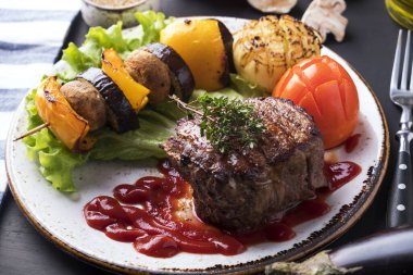 Kırmızı soslu sulu orta boy biftek ve tabakta ızgara sebze. Yakın çekim.