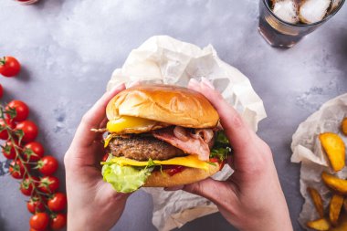 Kızarmış yumurta ve pastırma ile sulu sığır burger tutan kadın eller. Üst görünüm.