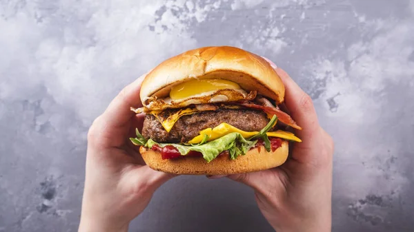Kızarmış yumurta ve pastırmalı lezzetli sığır burger tutan kadın elleri. Üst Manzara. Amerikan yemekleri.
