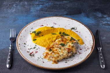 Peynirin altında fırında tavuk ve çatal ve bıçakla servis edilen havuç püresi..