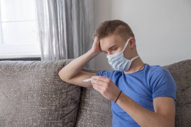 Hasta adam kanepede oturup evdeki termometreyle ateşini ölçüyor..