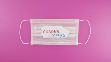 Koruyucu maske ve pembe arka planda CORONAVIRUS metni. Koronavirüsü durdurun. Üst görünüm