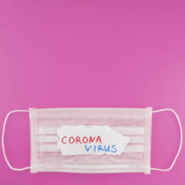 Cerrahi koruyucu maske ve pembe arka plandaki CORONAVIRUS metninin üst görüntüsü. Boşluğu kopyala, metin boşluğu