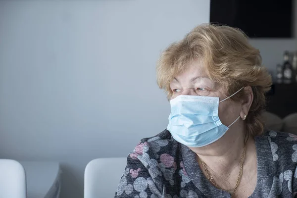 Mavi tıbbi koruyucu maskeli yaşlı kadın pencereye bakıyor. Karantina