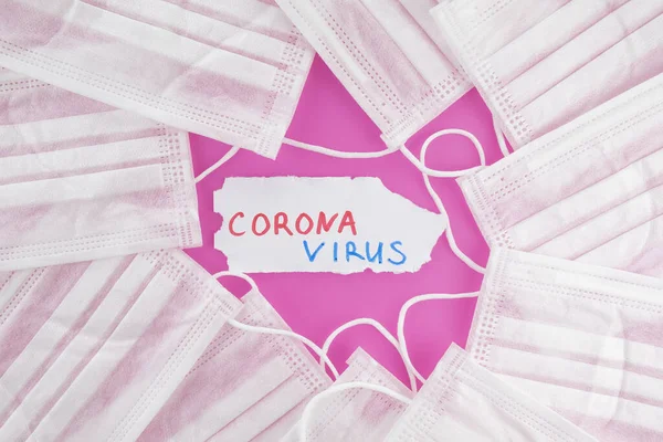 Coronavirus kavramı: koruyucu beyaz maskeler ve pembe arka planda CORONAVIRUS kelimesi. Üst görünüm