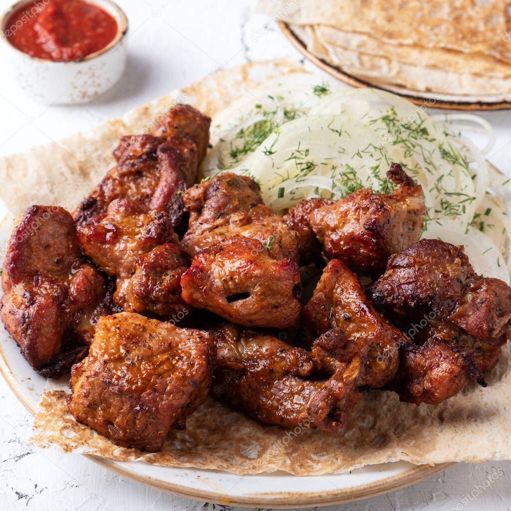 Meat shish kebab on a plate. Sashlik  with red sauce. Closeup