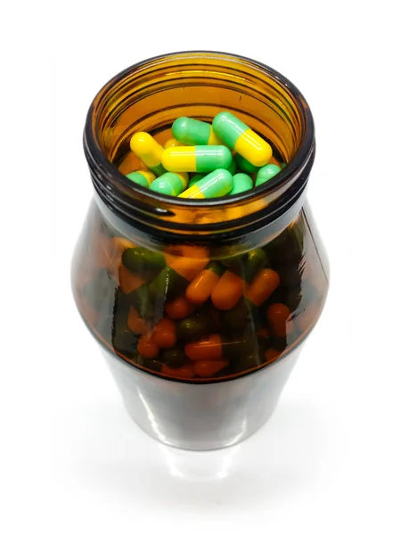 Капсулы и медицинская бутылка изолированные, желтые зеленые таблетки — стоковое фото